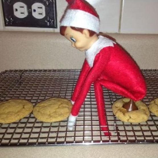 An elf squatting over cookies with a chocolate chip underneath