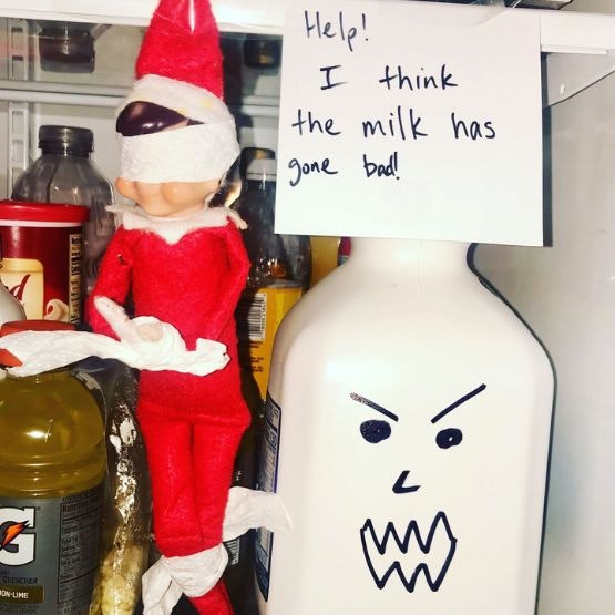 A blindfolded elf with a milk bottle with a scary face drawn on and a sign saying 