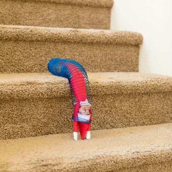 An elf in a slinky coming down the stairs upside down