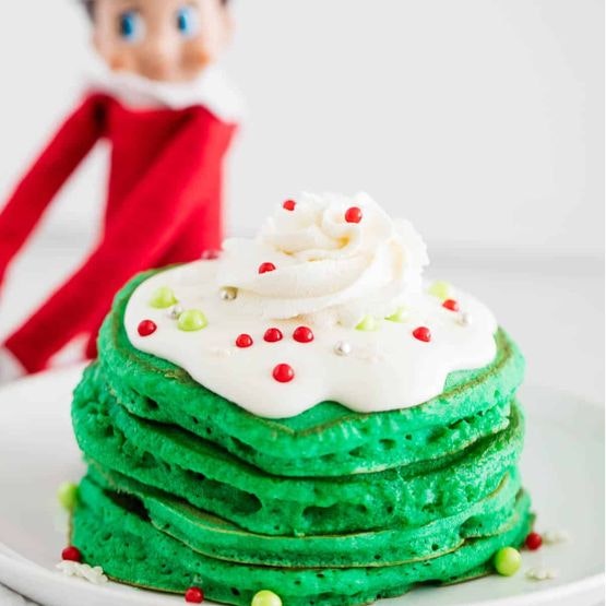 An elf behind a plate of green pancakes