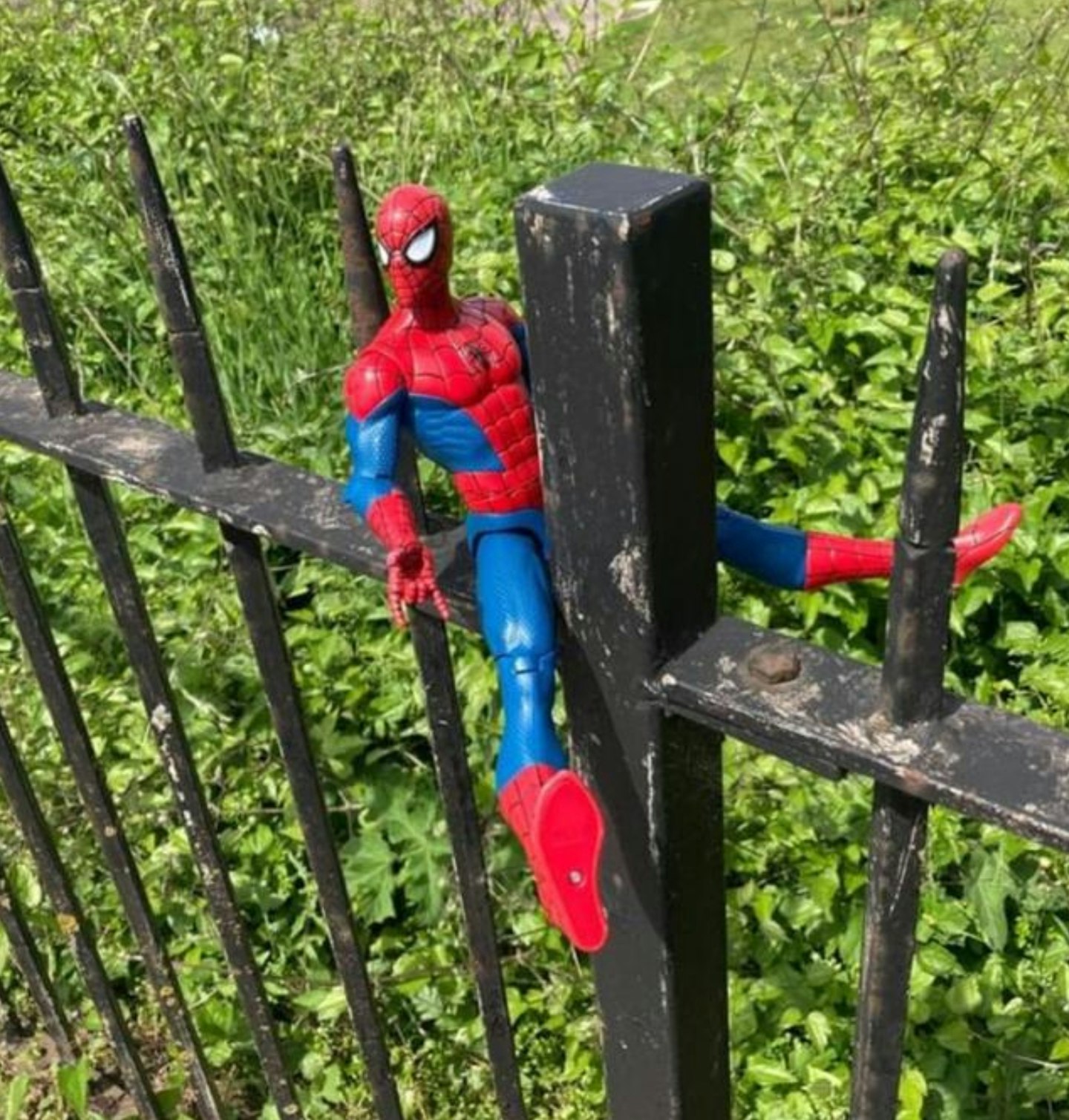 Spider-man action figure sitting on a gate, placed by a child..
