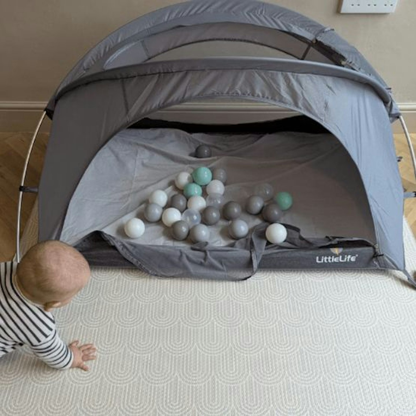 The LittleLife Arc 2 travel cot filled with balls as a play pen with a baby crawling towards it