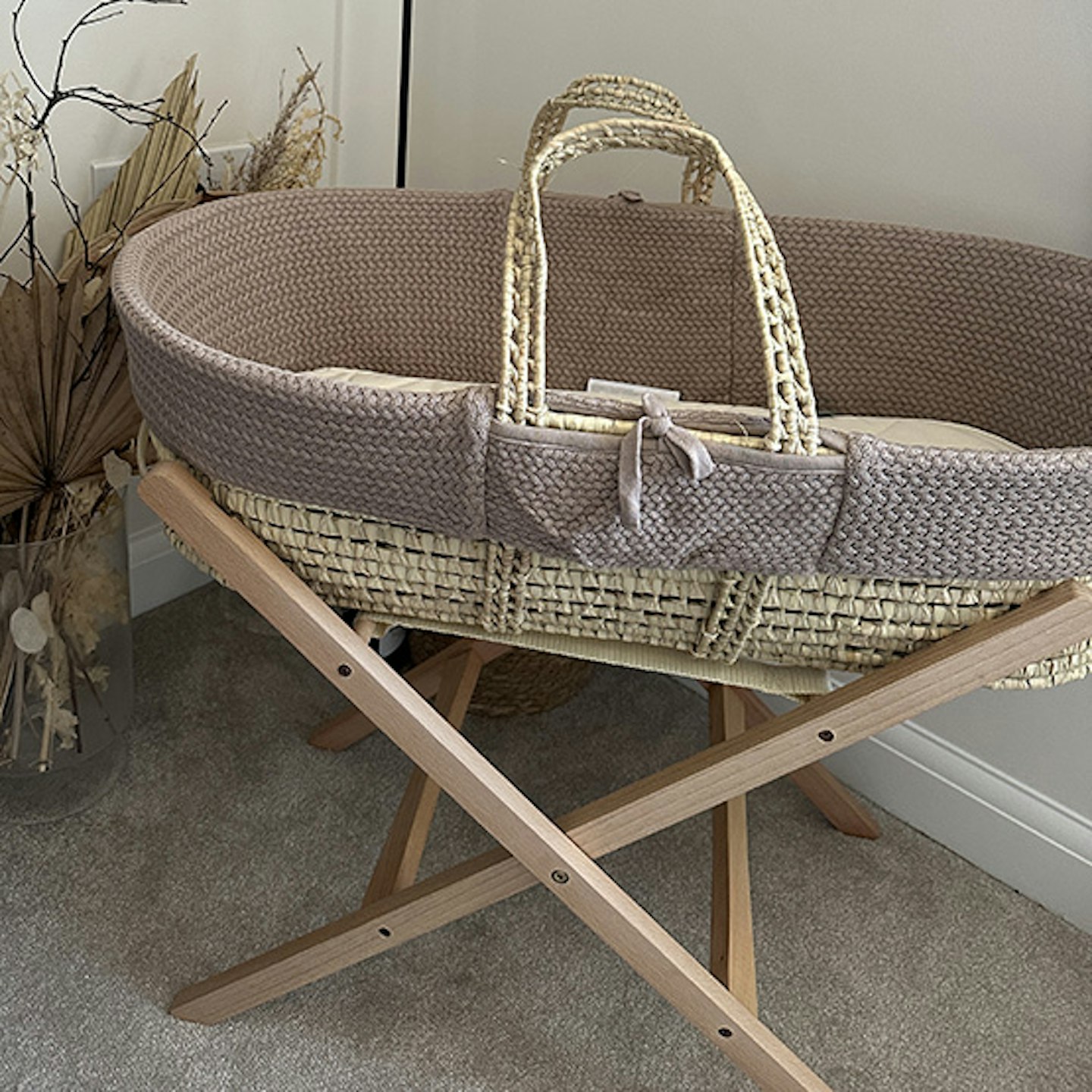 The Little Green Sheep Natural Knitted Moses Basket and Mattress in the corner of a room