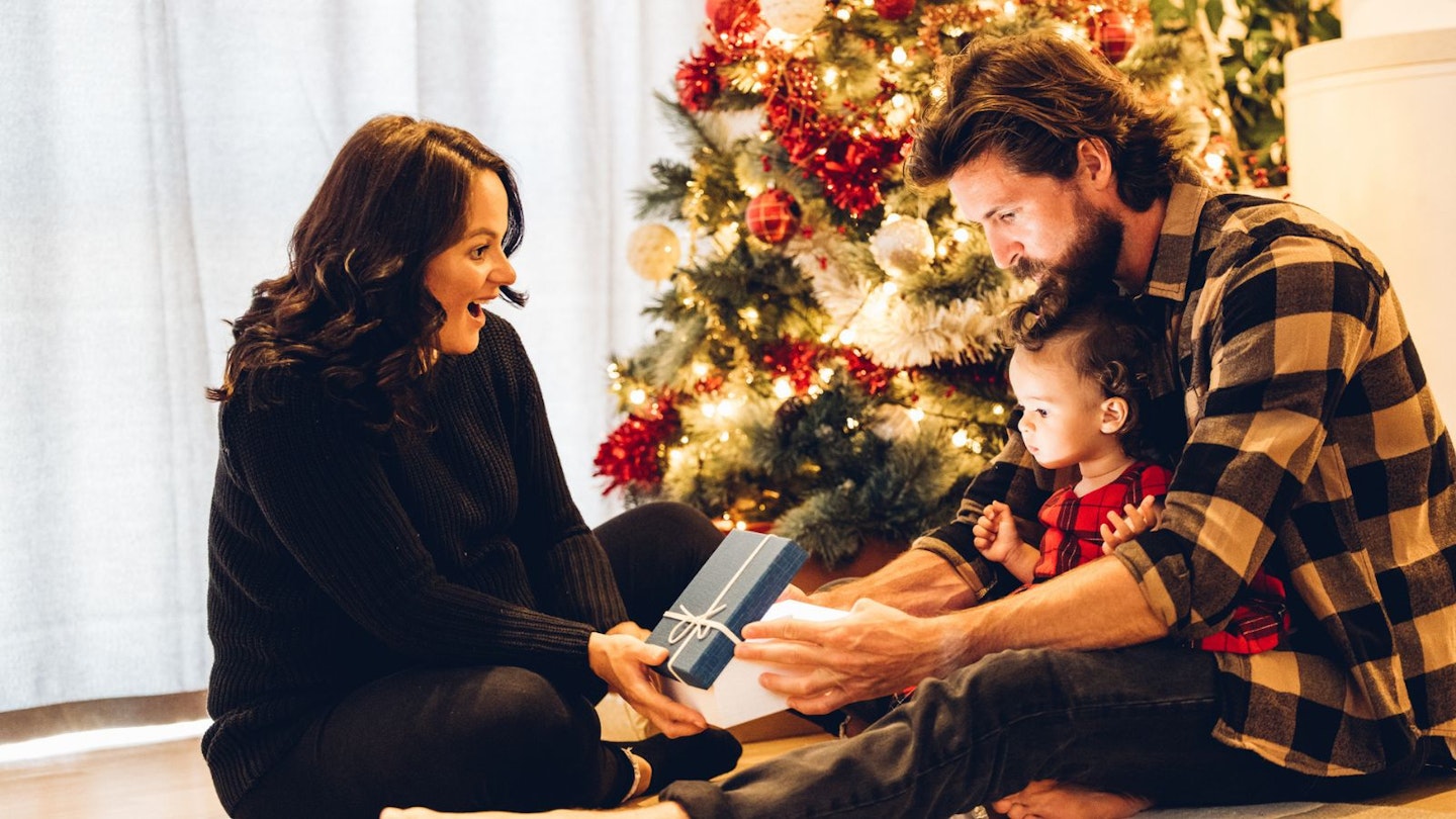 Two parents giving a child a Christmas present next to the tree
