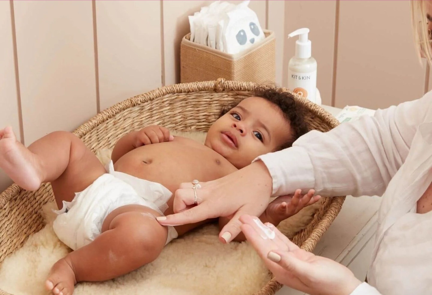 A mother gently applying lotion to her baby who is lying down.