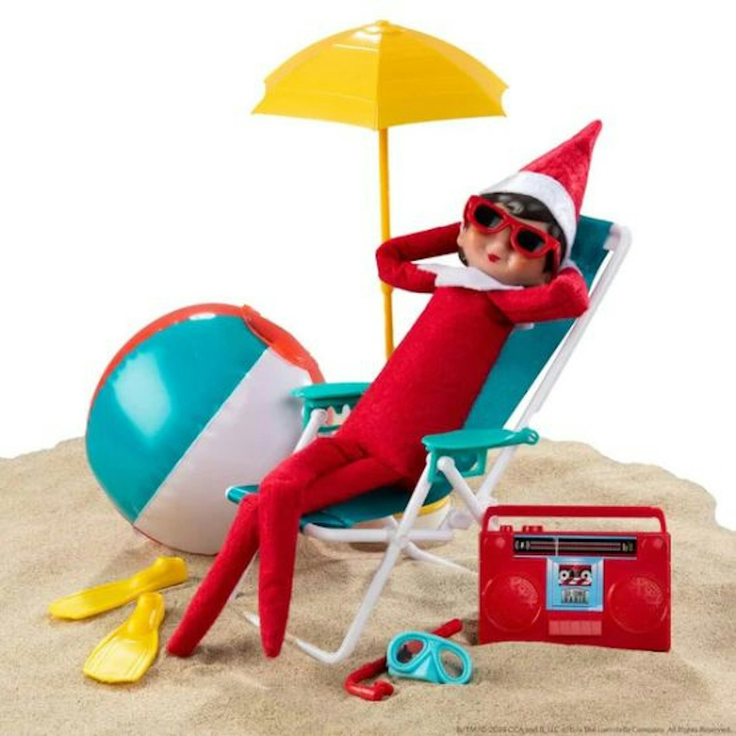 An Elf lying on a deck chair on sand with sunglasses on, an umbrella, beach ball, boombox and flippers