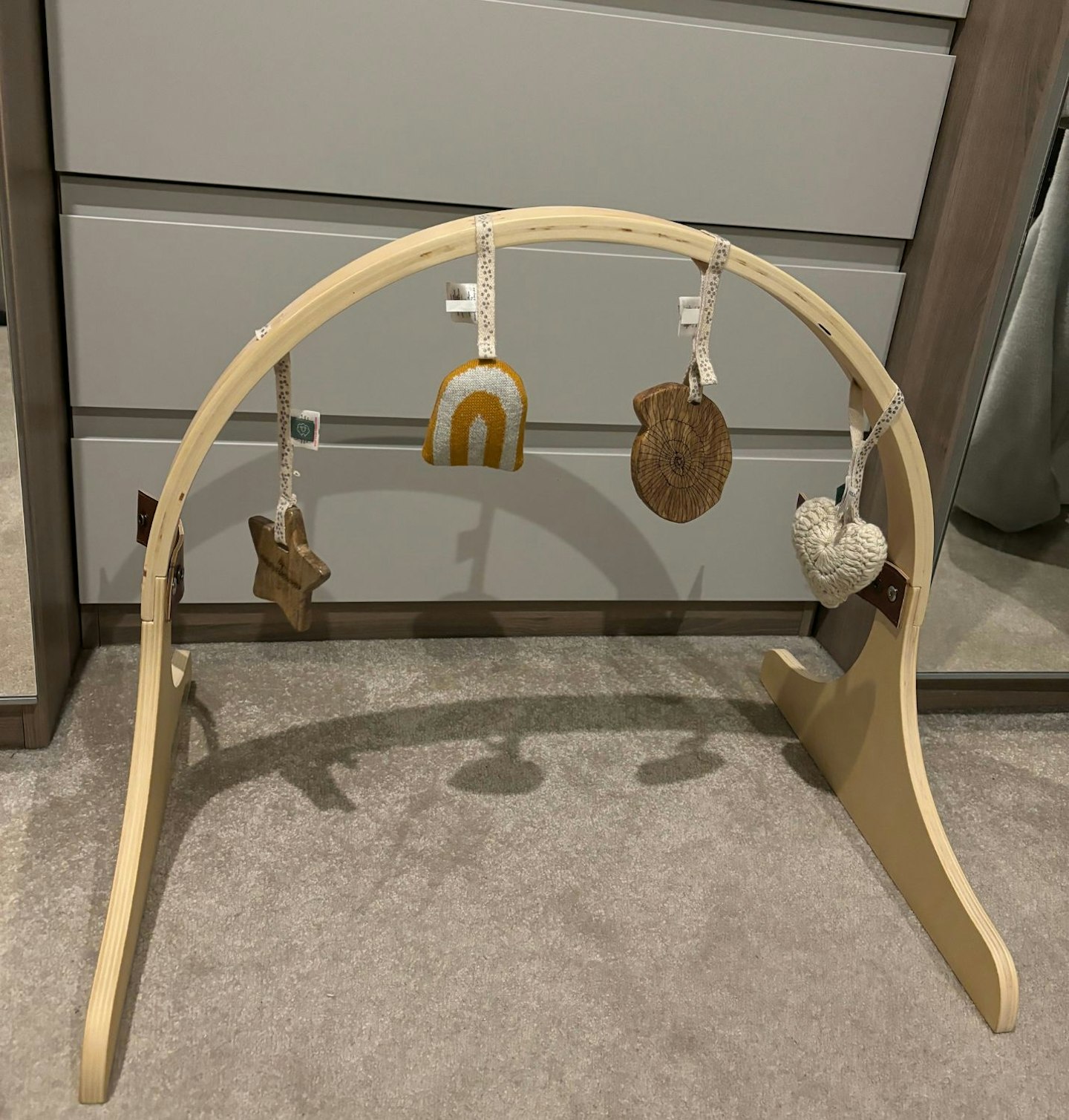 Photograph of a natural wood arch for baby play mat in a neutral bedroom