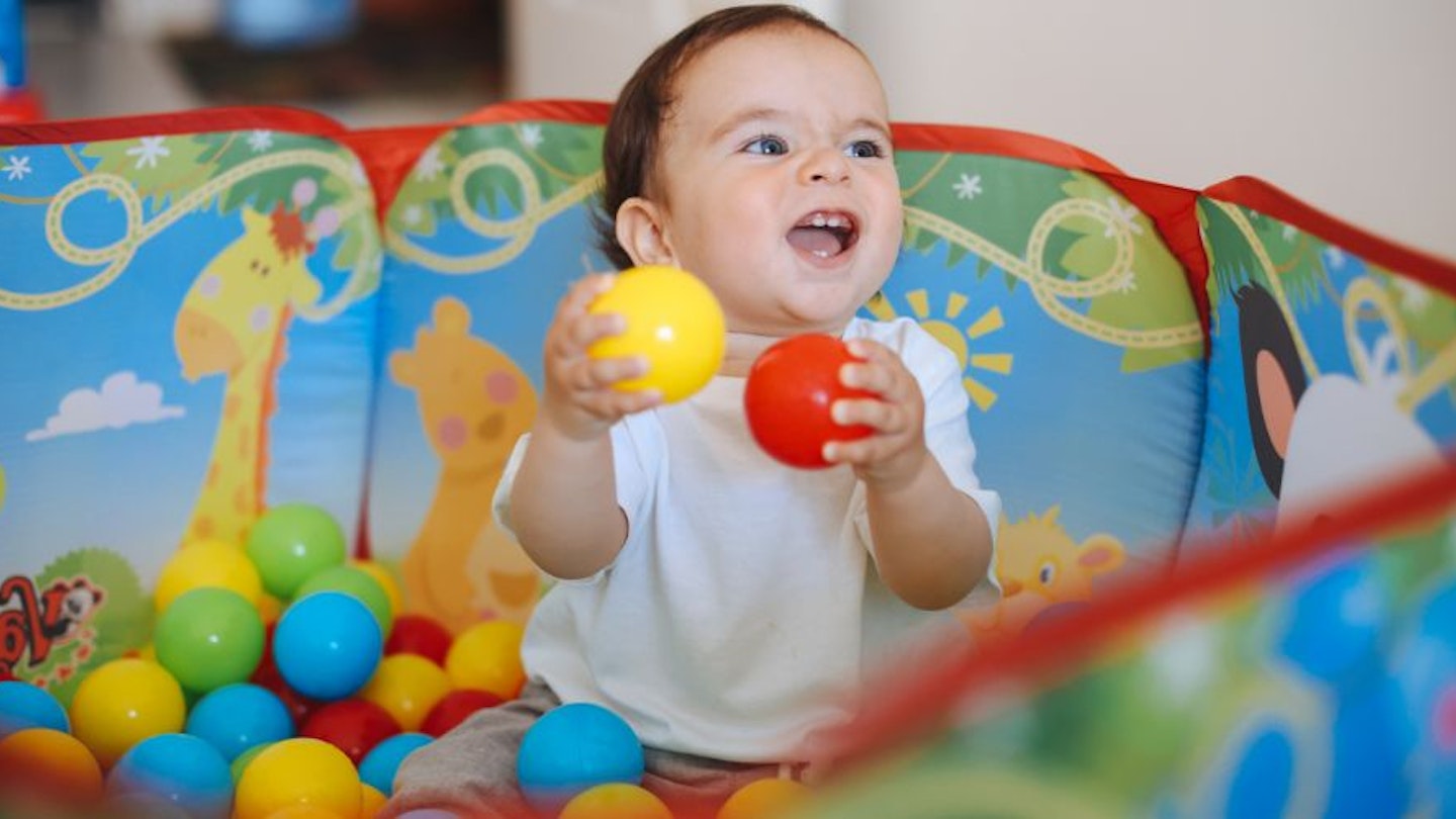A baby sat in a ball pit holding two balls