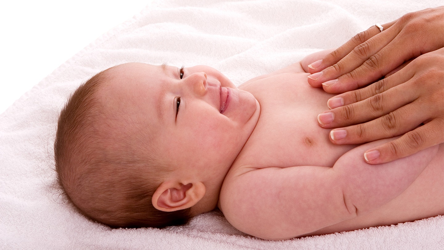 A baby laying on a bed smiling at their caregiver.