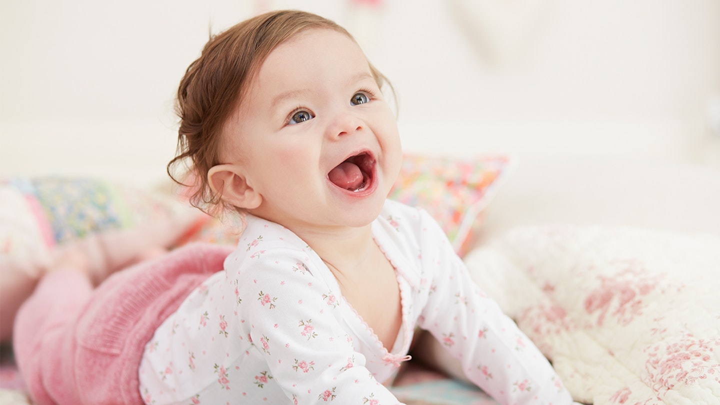 A baby girl wearing pink with a huge grin, smiling.