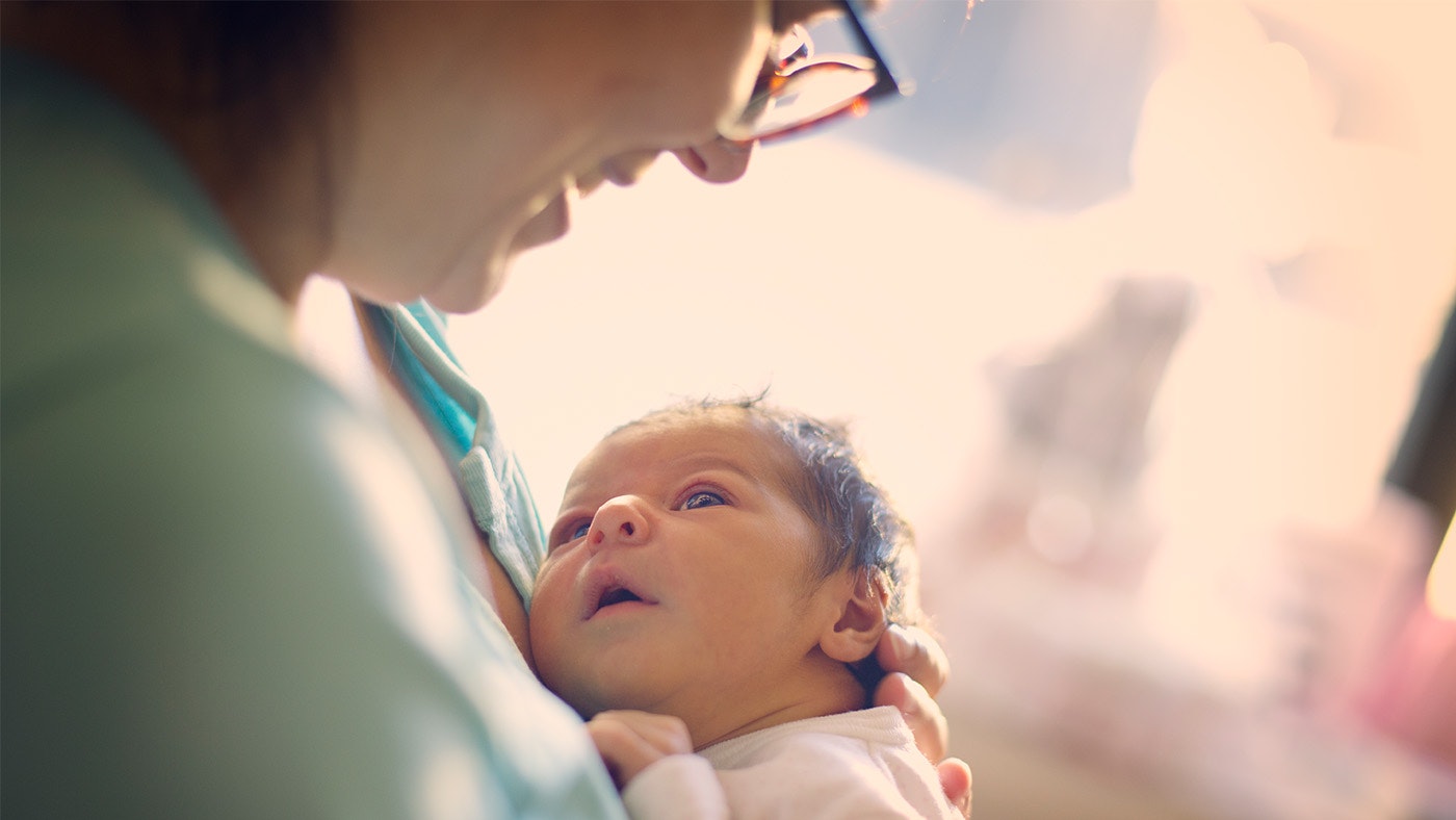 A mother holding her baby and looking down into its eyes, while it looks up at her