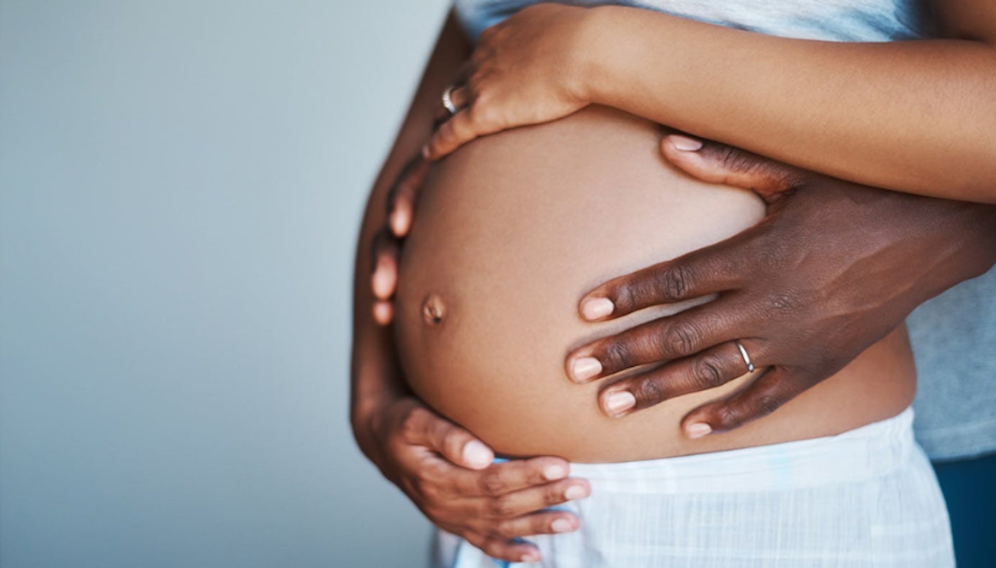 Couple standing together hugging pregnant woman's bump