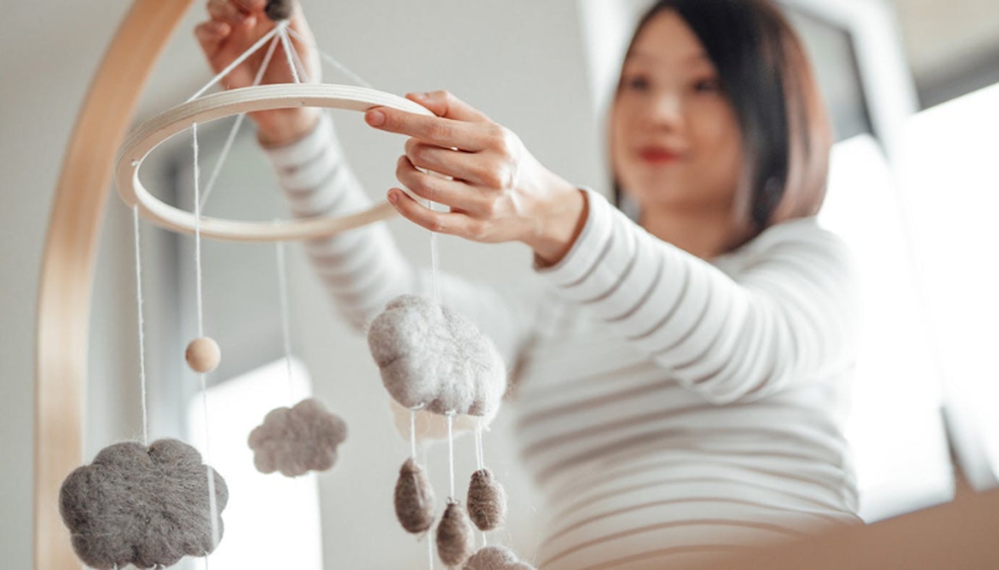 Pregnant woman adjusting a child's crib mobile