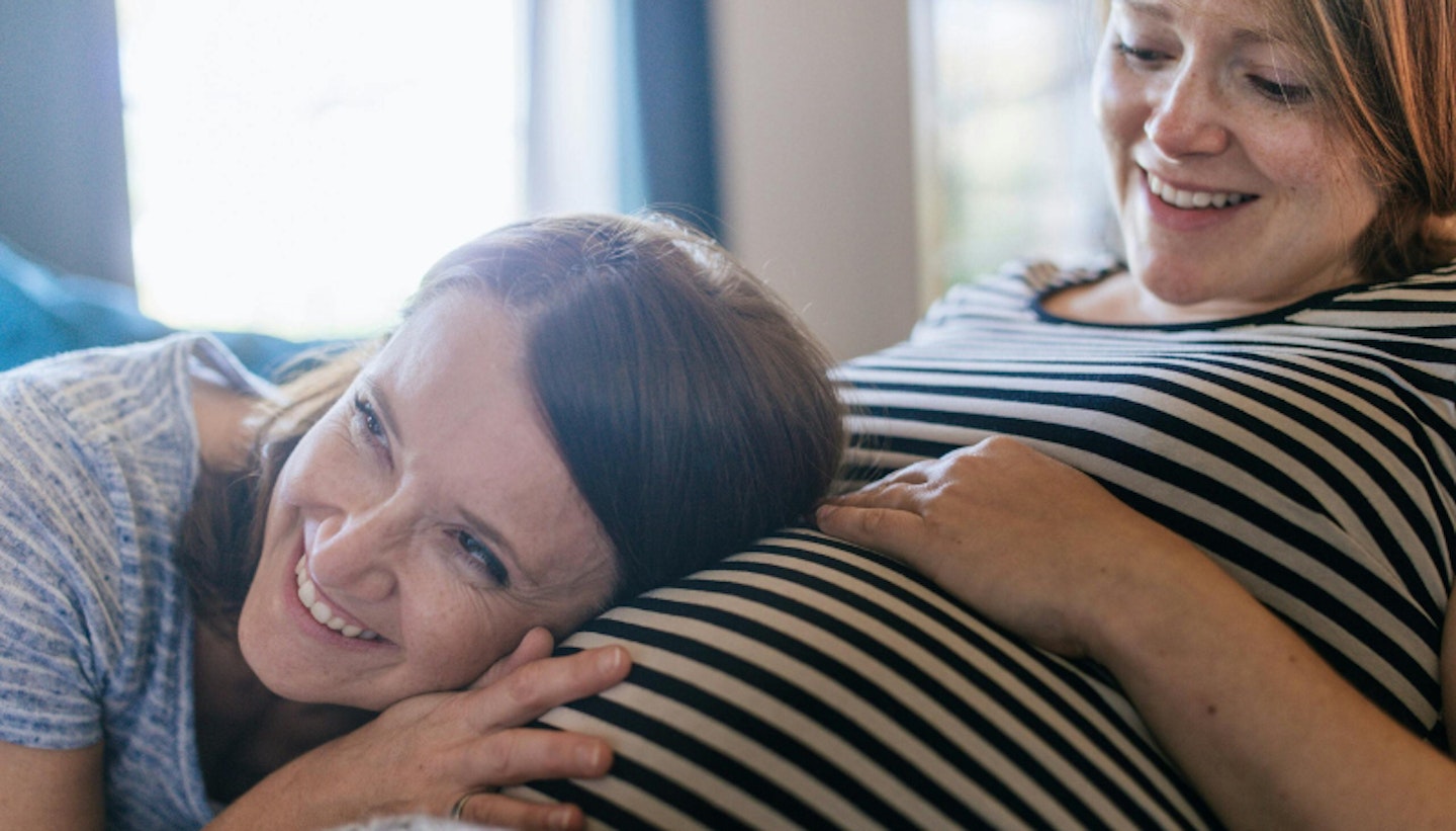Woman with her ear to a pregnant woman's bump