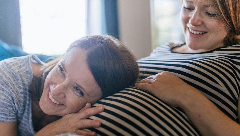 Woman with her ear to a pregnant woman