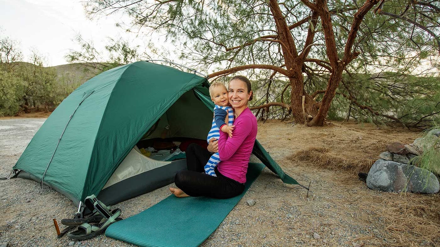 Mum holding toddler in front of a tent