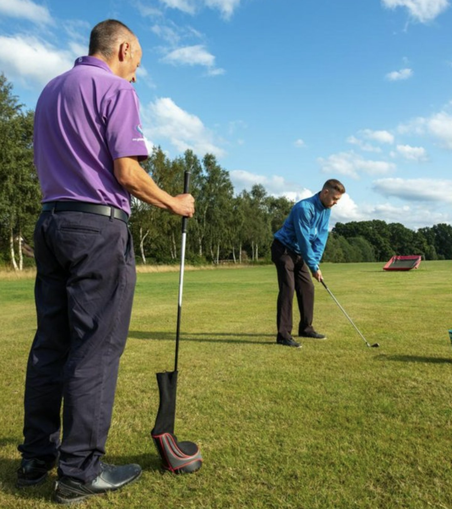 An image of two men playing golf outside with lush green grass and blue skies