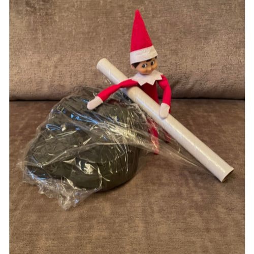 An Elf on the Shelf wrapping a pair of shoes in cling film