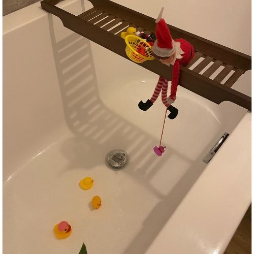 An elf hanging off a bath caddy with a fishing rod and rubber ducks