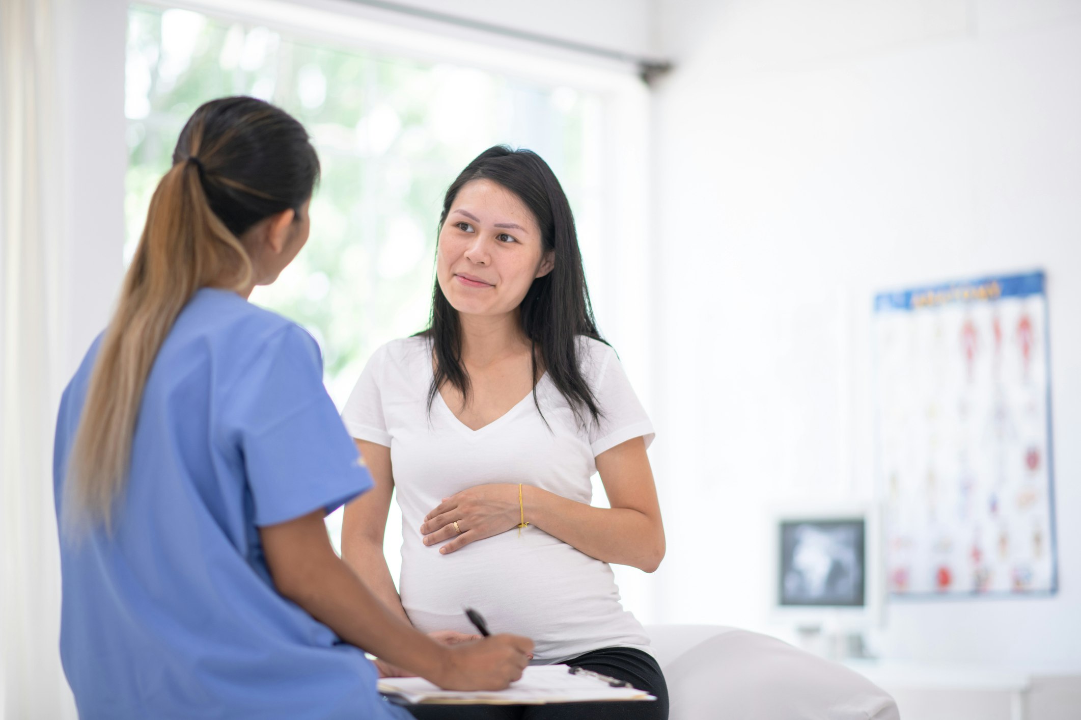 A pregnant woman smiles as she talks to her nurse in the doctor