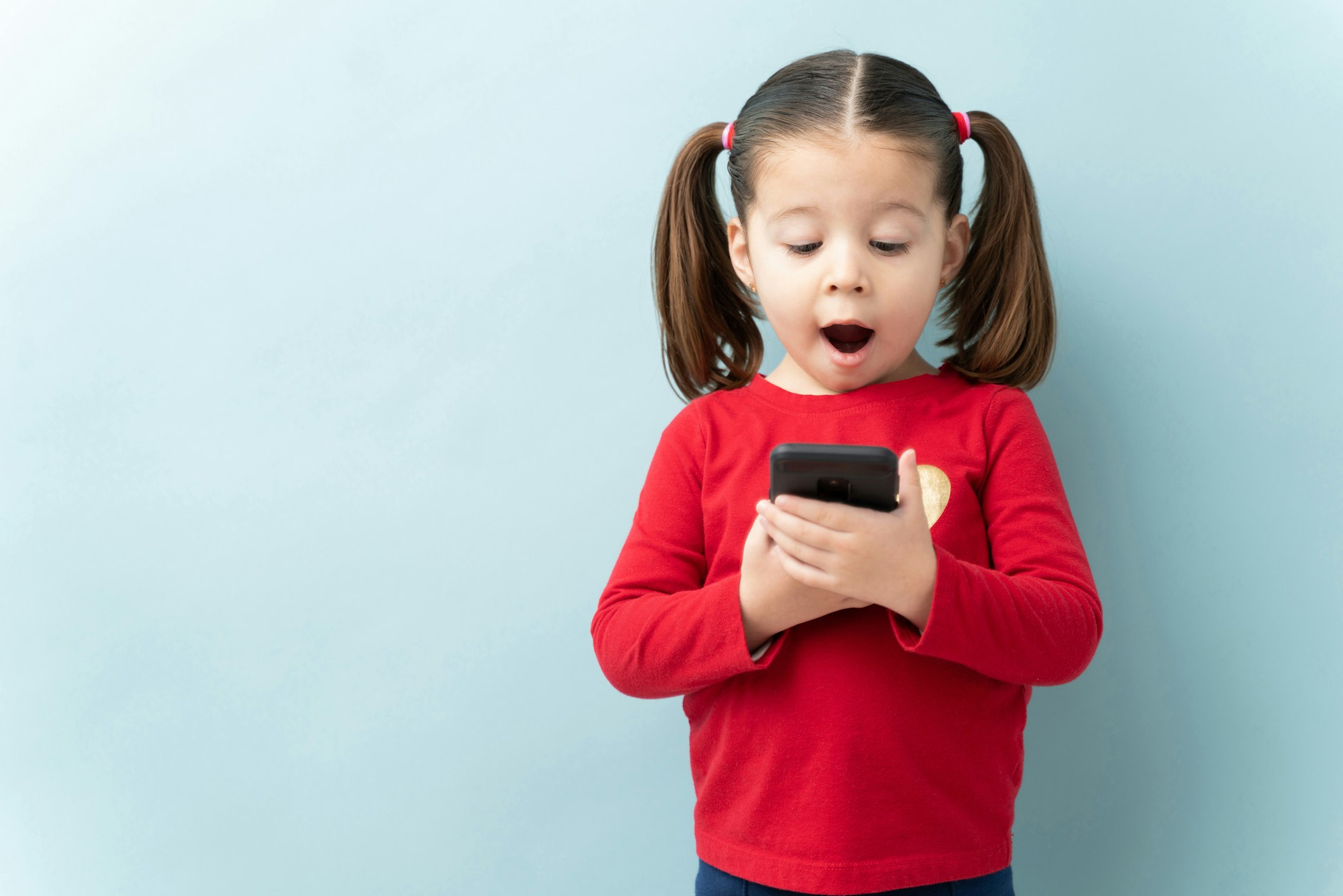 little girl holding a smartphone and looking surprised with her mouth open