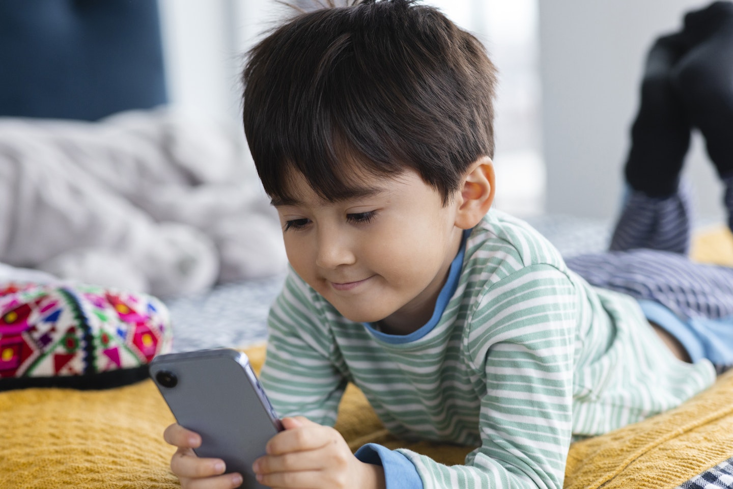 A little boy lying on a bed as he plays on a smartphone.