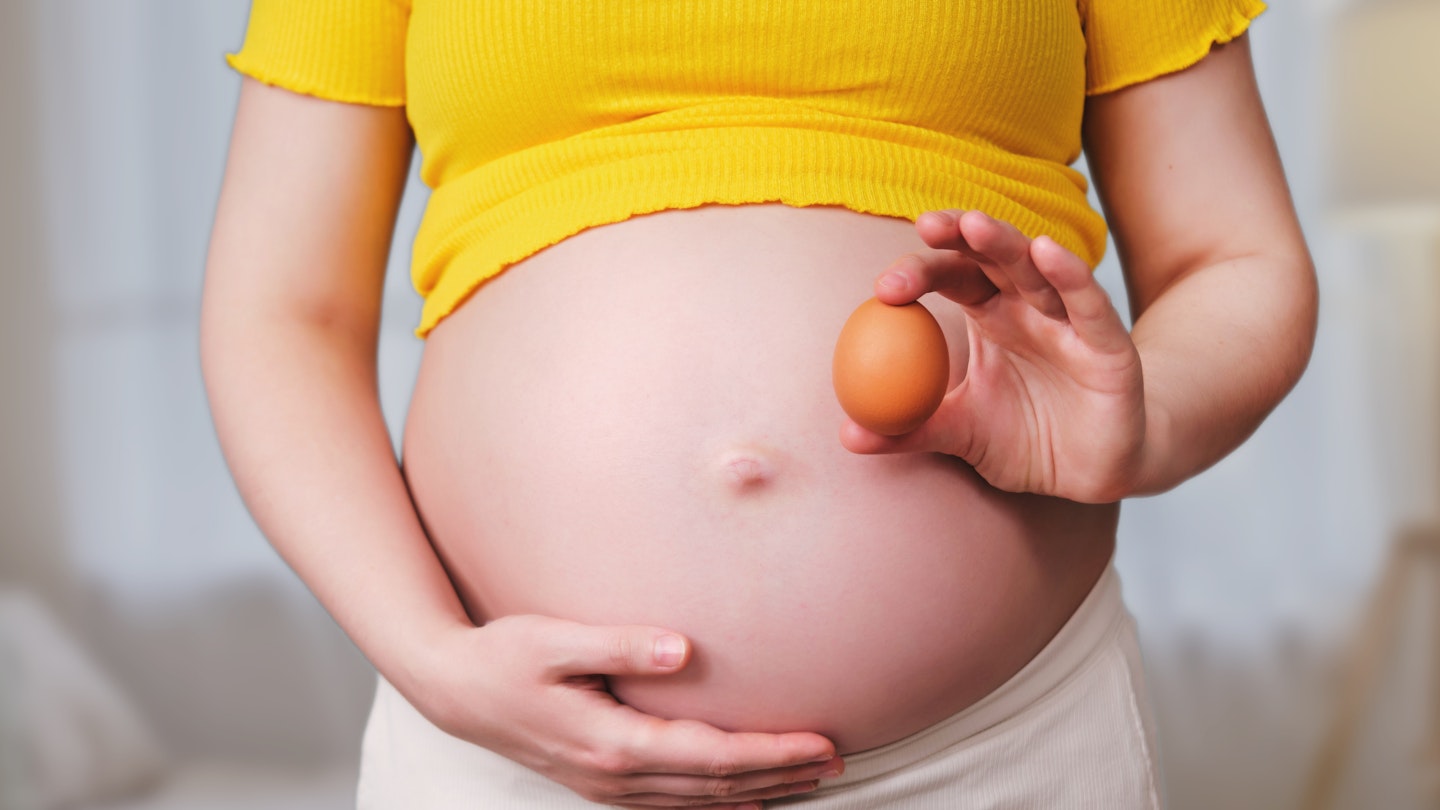 A pregnant woman holds a chicken egg in her hand