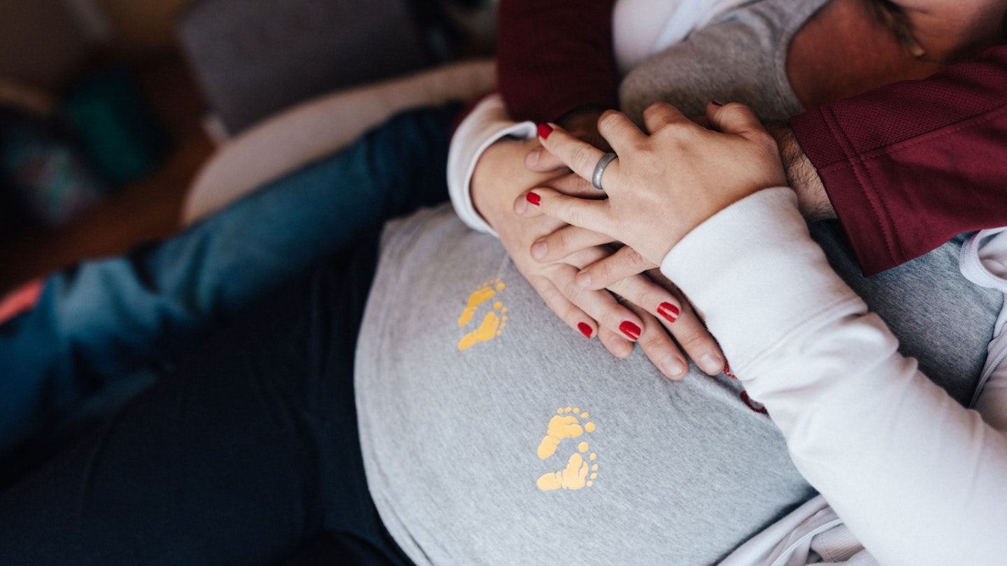 Couple holding pregnant belly with twin hearts