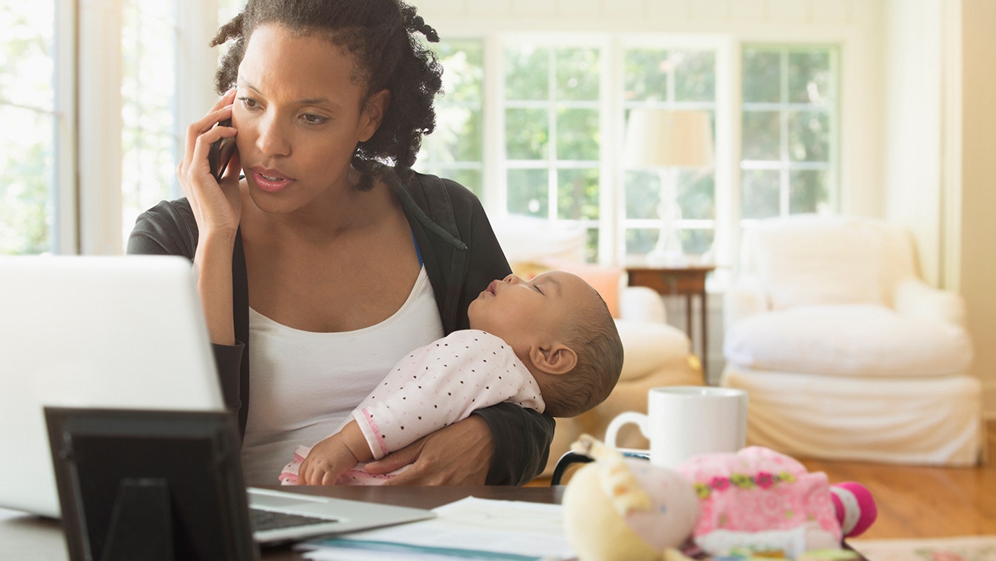 Mother holding baby and working in living room