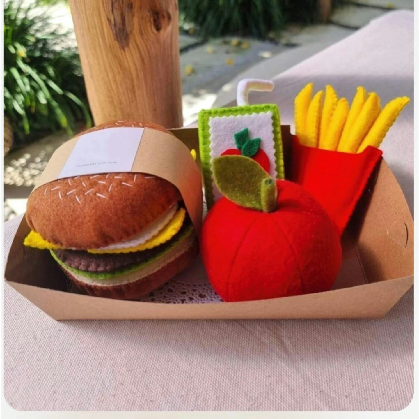 Happy Meal play food set made from felt with a burger and removable fillings, packet of removable chips, carton of apple juice and an apple in an eco-friendly cardboard container