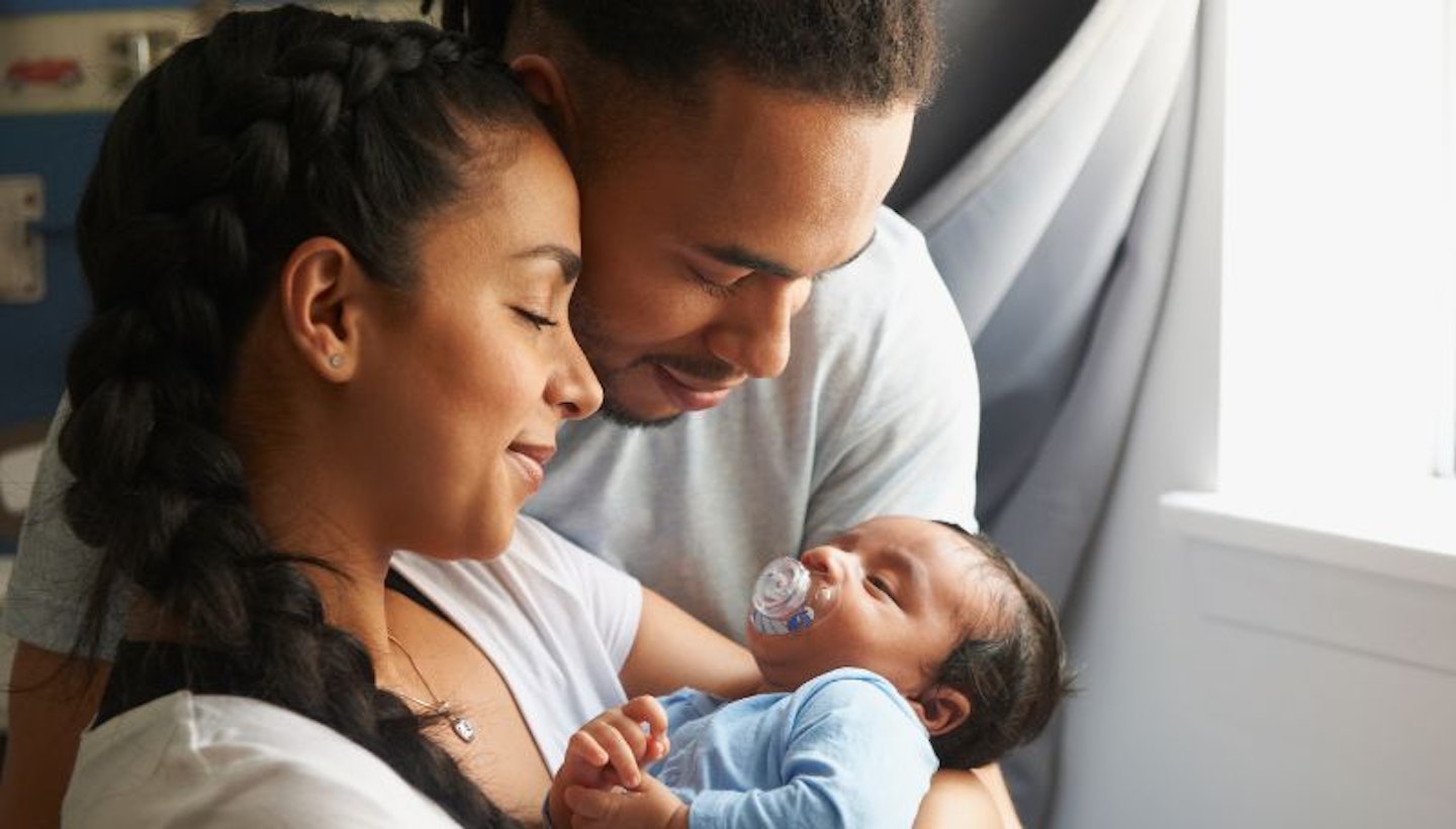 Couple cuddling a newborn baby with a dummy