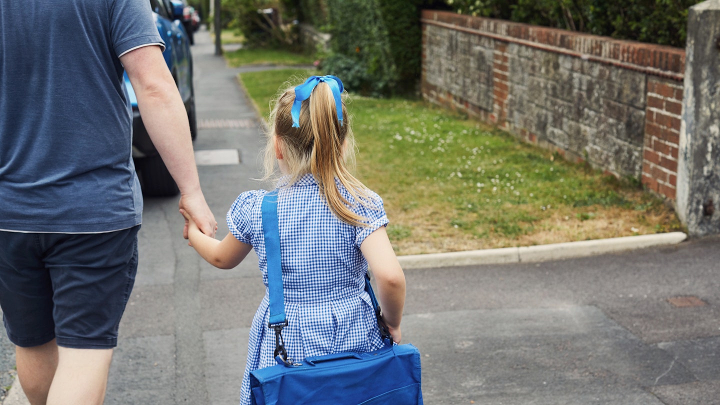 Parent and daughter walking to school in school uniform