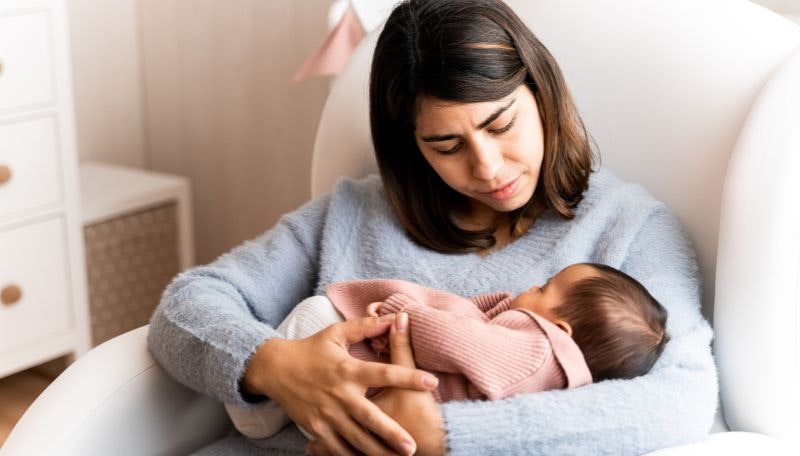 Mother sitting on soft chair holding newborn baby in her arms