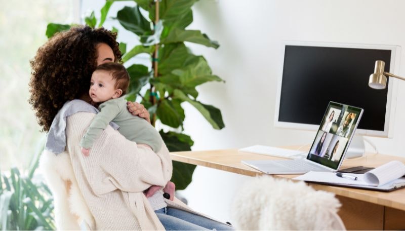 Mother working on laptop holding newborn baby over her shoulder