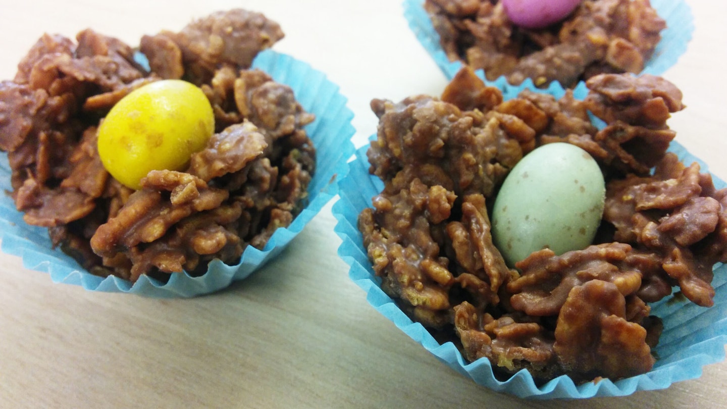 Cornflakes covered in milk chocolate, topped with a miniature easter egg, in blue cupcake casings.