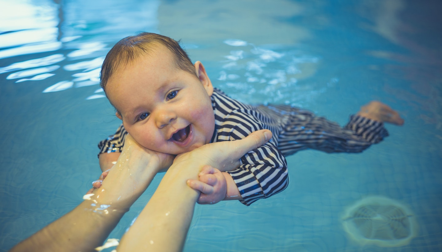 baby smiling while learning how to swim in the pool