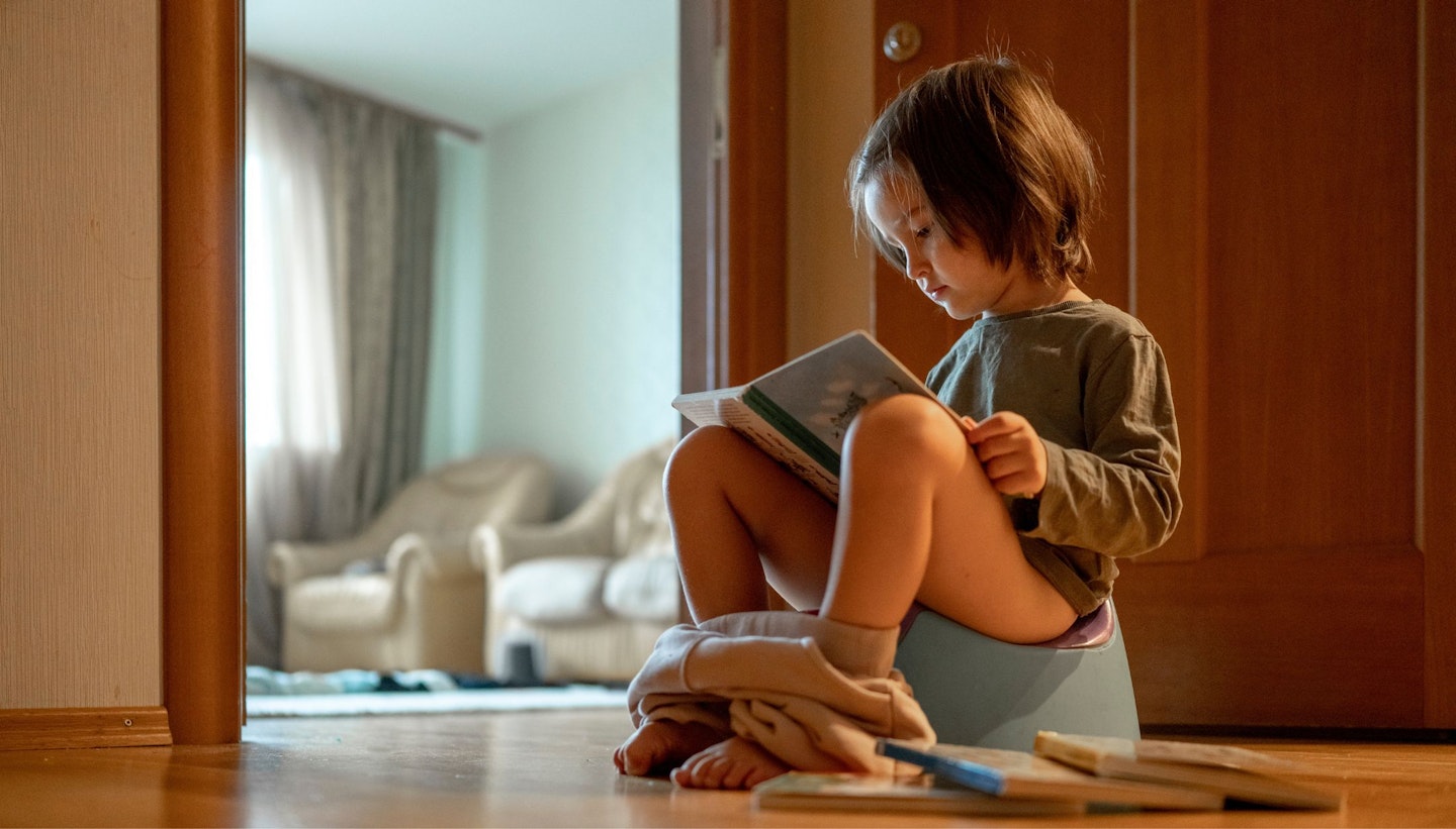 Cute boy sitting on potty and reading book at home