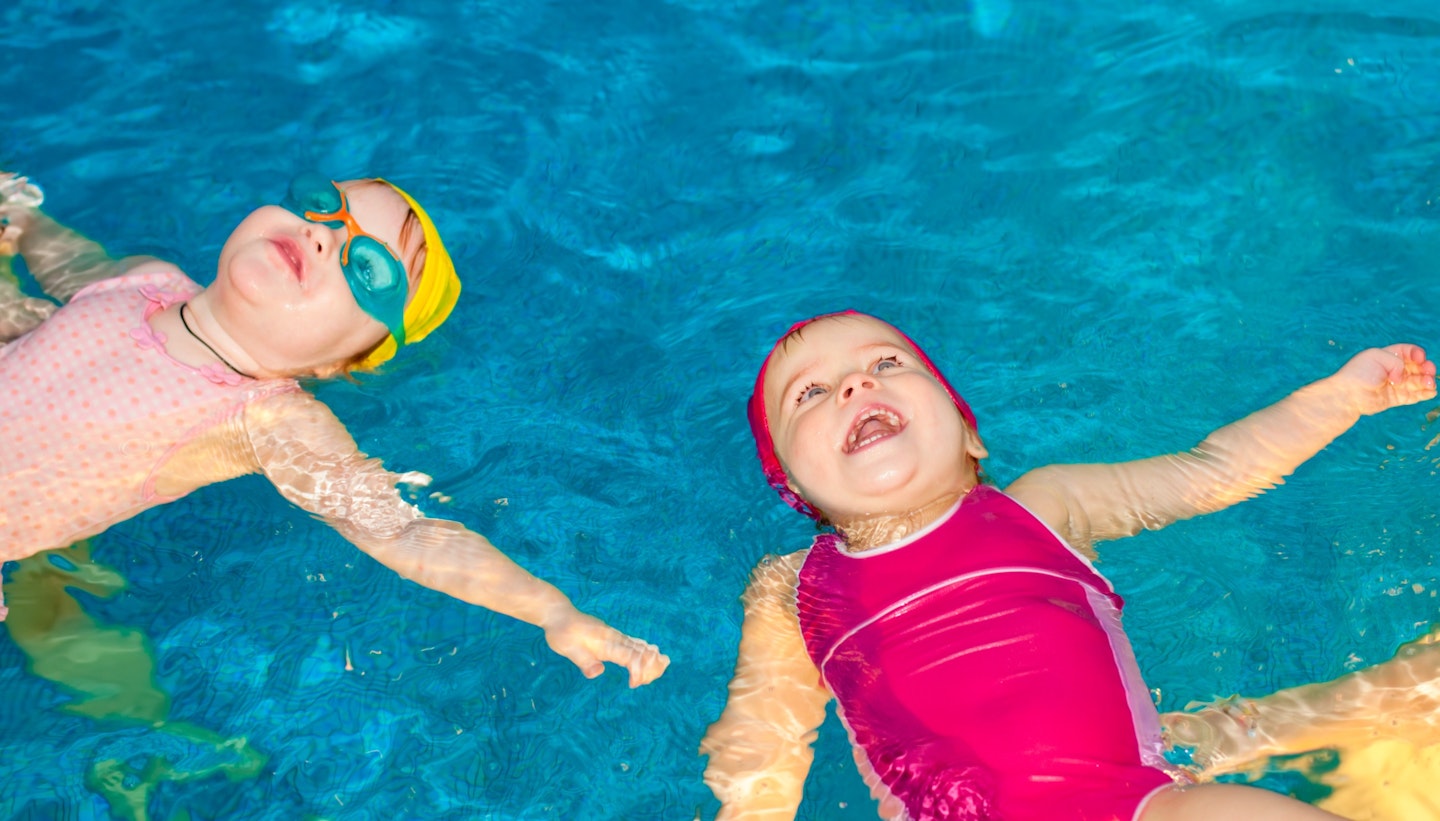 two toddlers in colourful swimming outfits floating on their backs in the pool
