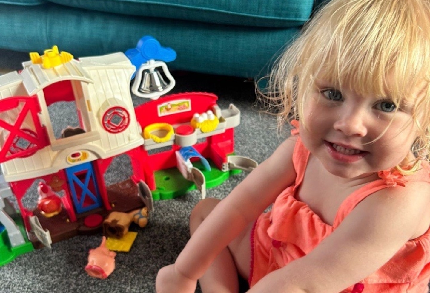 young girl sat on the floor, in front of the Fisher-Price Little People Caring for Animals Farm