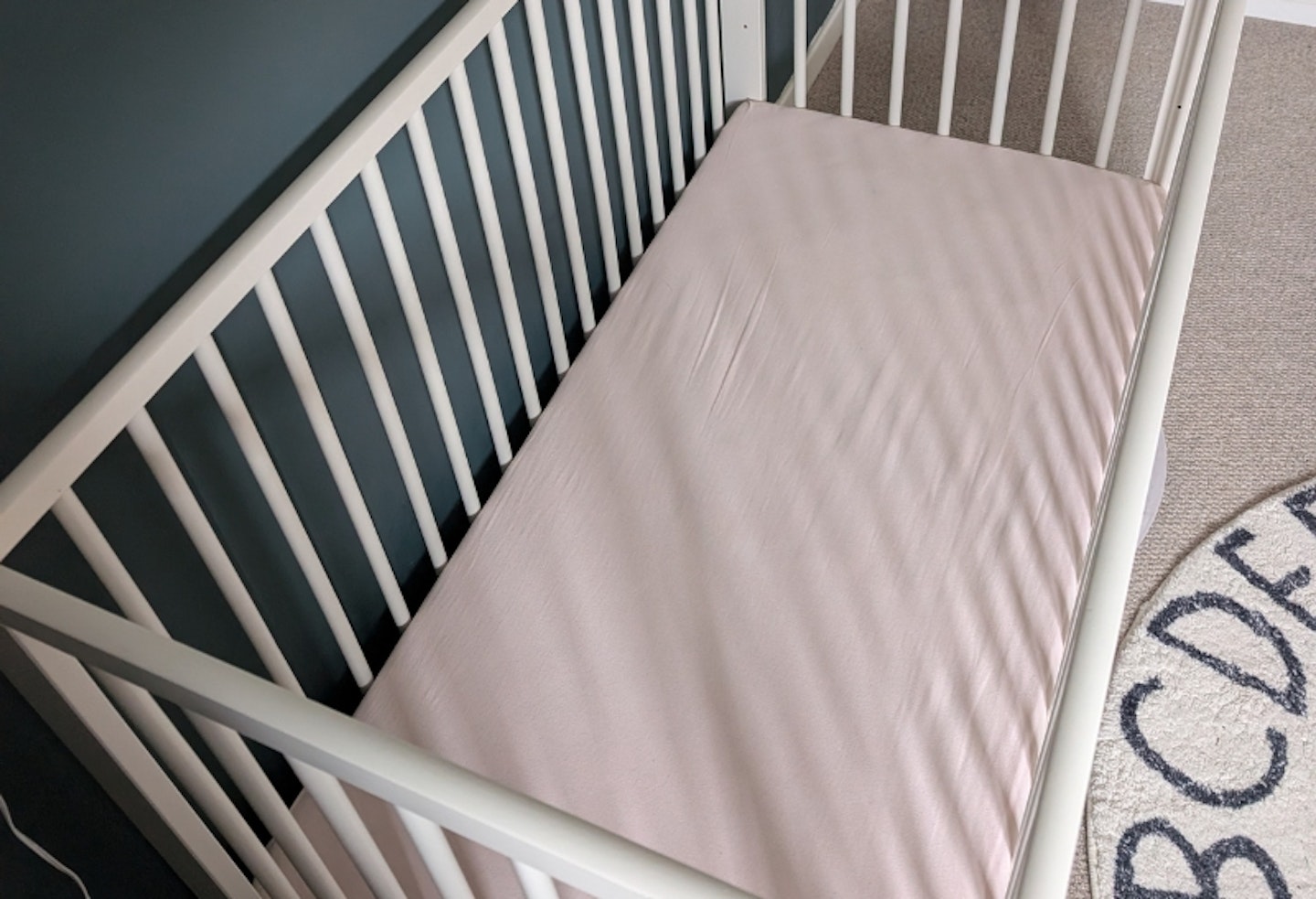 Tutti Bambini Sprung Cot Bed Mattress with a pink mattress cover on and in a white cot