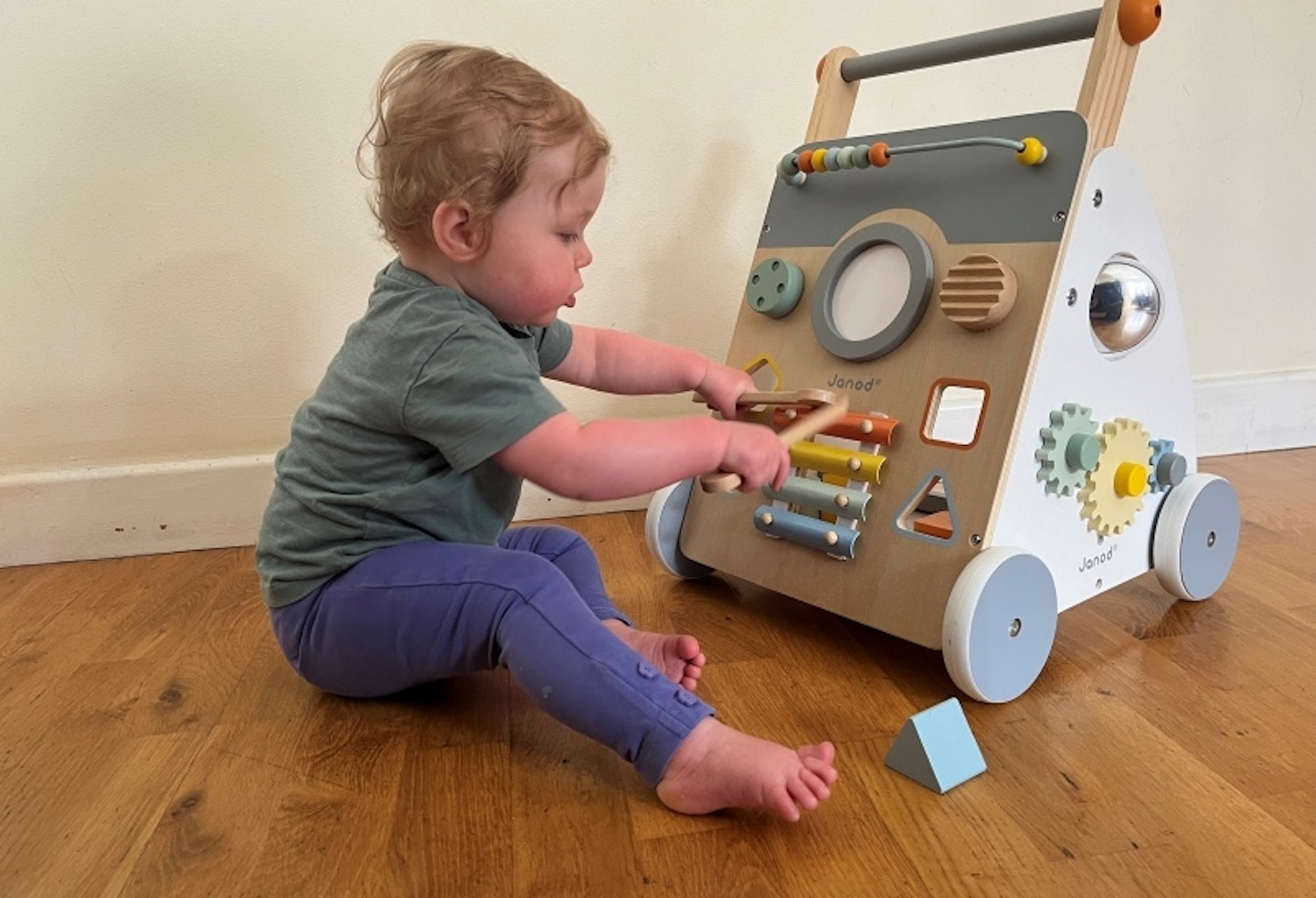 Toddler sitting on wooden floor playing on the xylophone with wooden mallet on the Sweet Cocoon Wooden Multi-Activity Baby Walker.