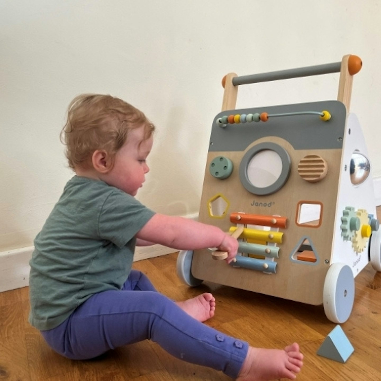 Toddler sitting on wooden floor playing with the Sweet Cocoon Wooden Multi-Activity Baby Walker