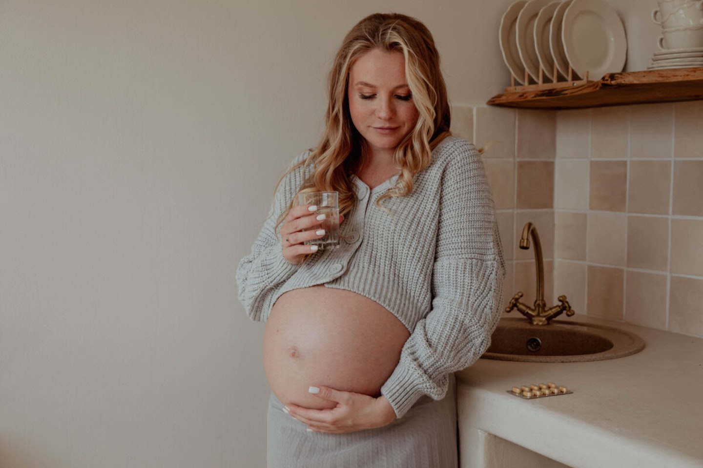 Pregnant and Aspirin use: a pregnant woman drinking a glass of water with pills on the kitchen counter