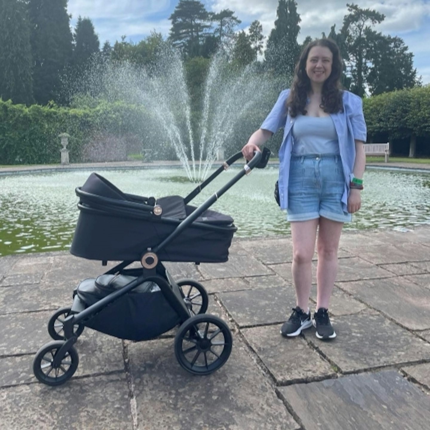 Woman standing with the Ickle Bubba Altima travel system holding the handle