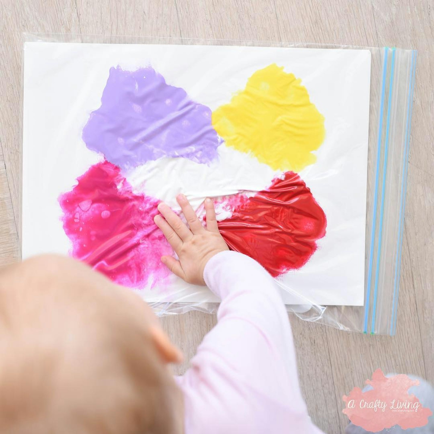 baby enjoying sensory play with a zip-lock bag filled with coloured paint