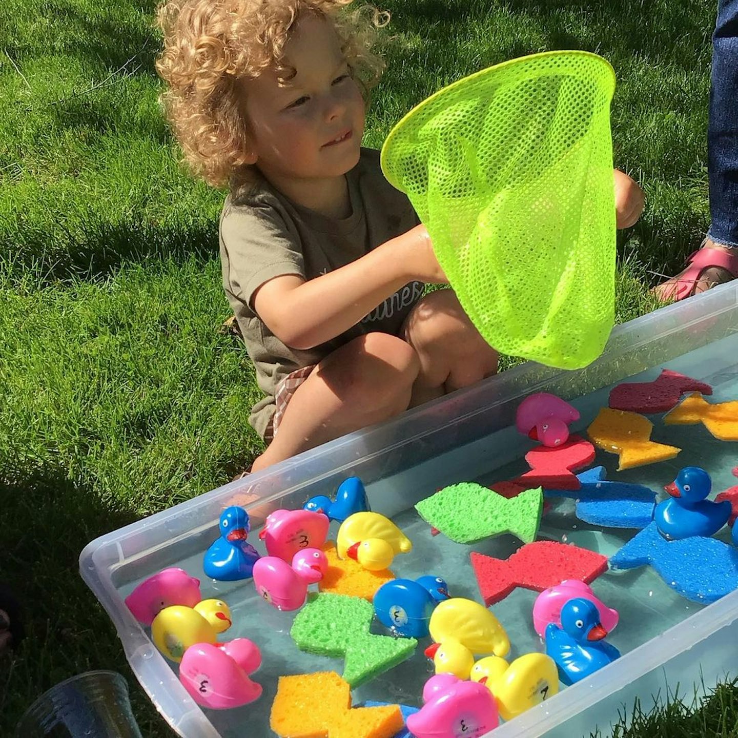 Child fishing for sponge fish on contaihner of water for sensory play