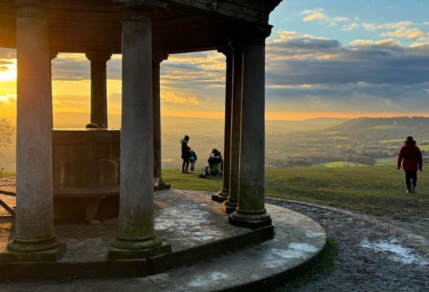 A structure on top of a hill, with people silhouetted by the sun setting behind