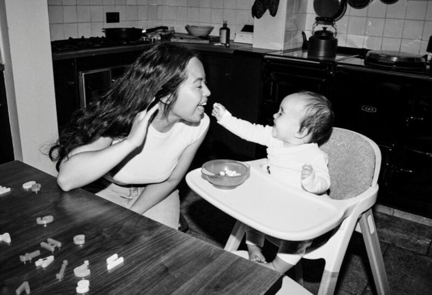 Mother laughing while her baby feeds her from its highchair