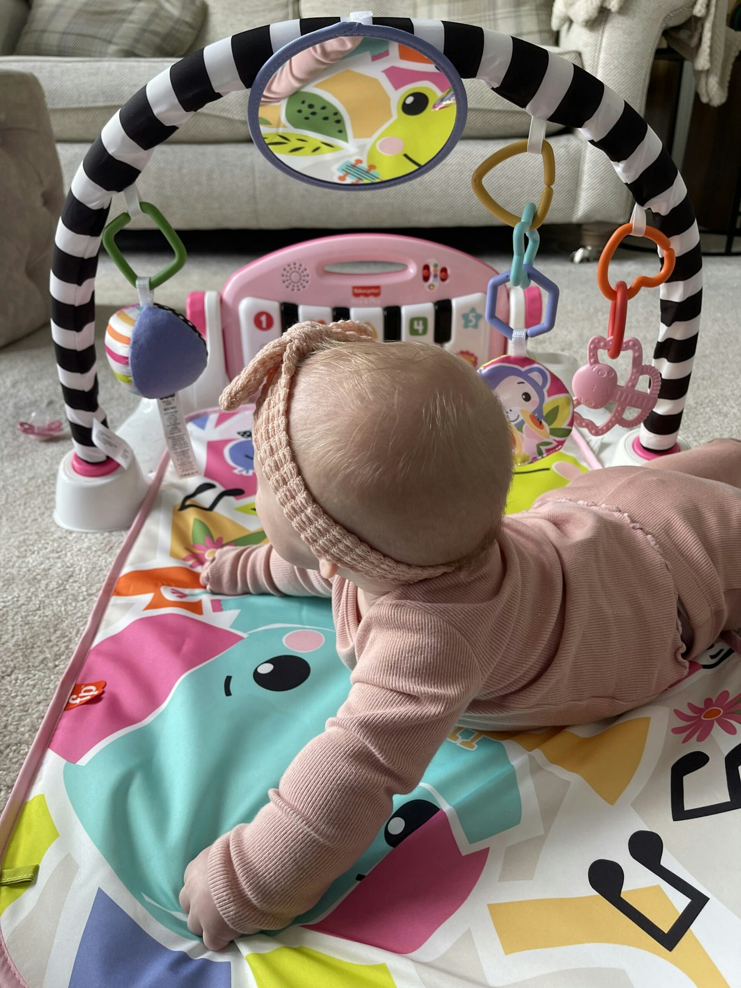 Baby playing on their front on colourful baby play mat and activity play gym by Fisher-Price with play piano and hanging animal toys