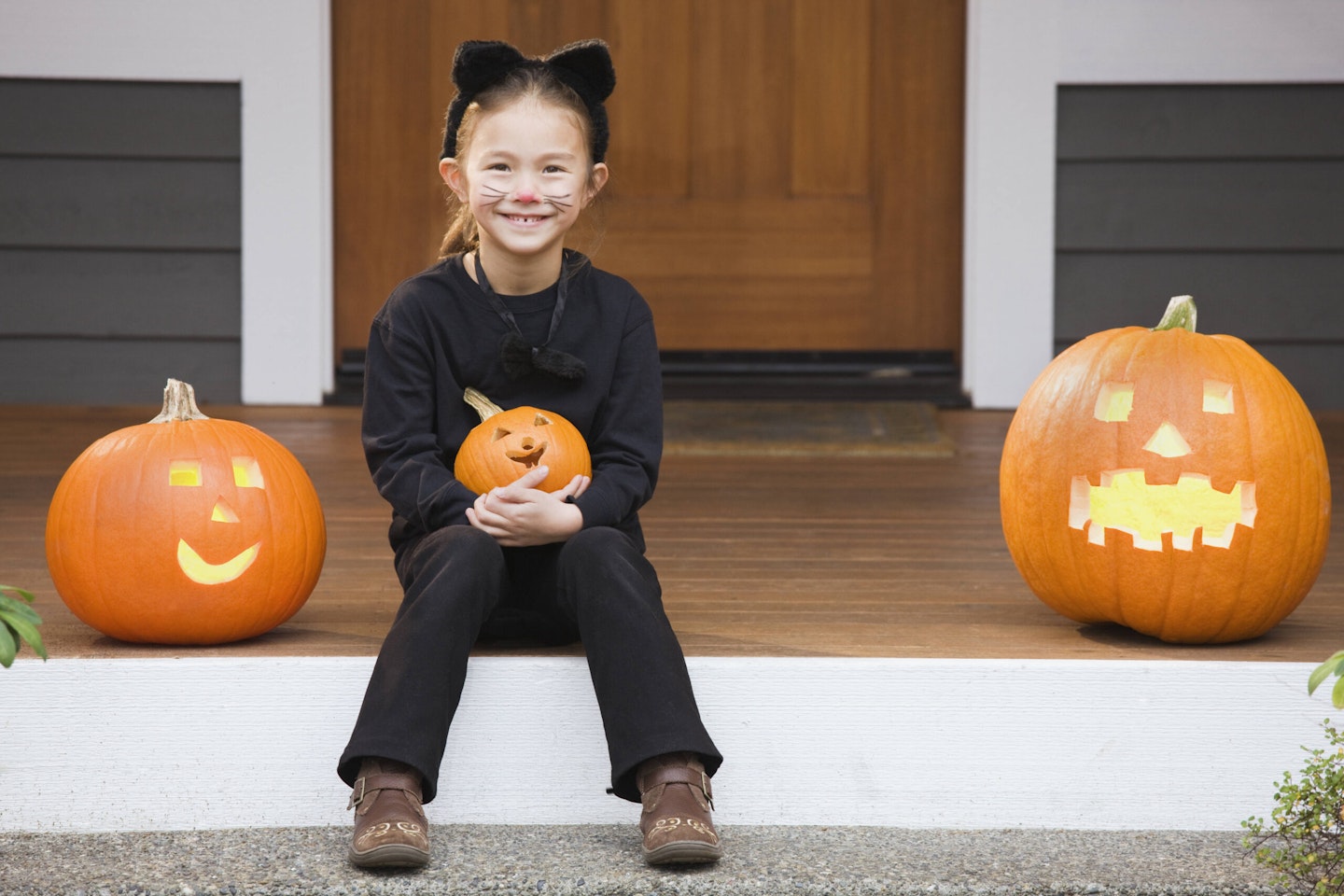 Little girlin cat costume with cat Halloween face paint holding a pumpkin